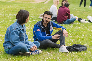 Students socialising outside on campus while sitting on grass
