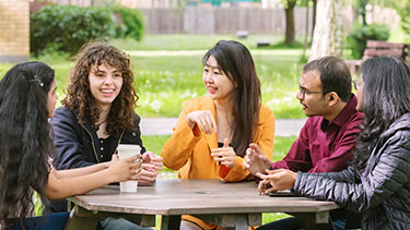 Group of students socialising on table outside on campus
