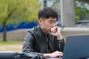 Male student on laptop outside on campus